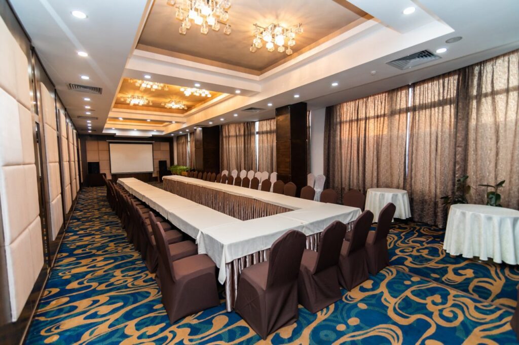 Conference room with a U-shaped table arrangement, brown chairs, patterned blue and gold carpet, and a projection screen at the front