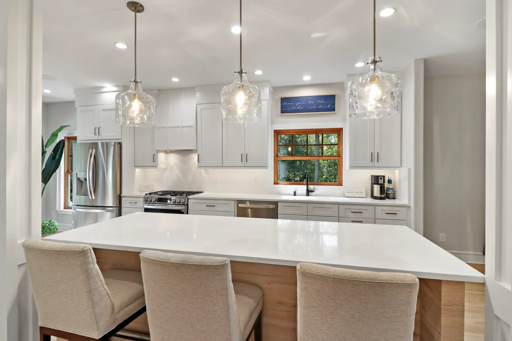 Modern kitchen with white cabinets, a large island with three bar stools, and a sign above the window reading Love you to the lake and back