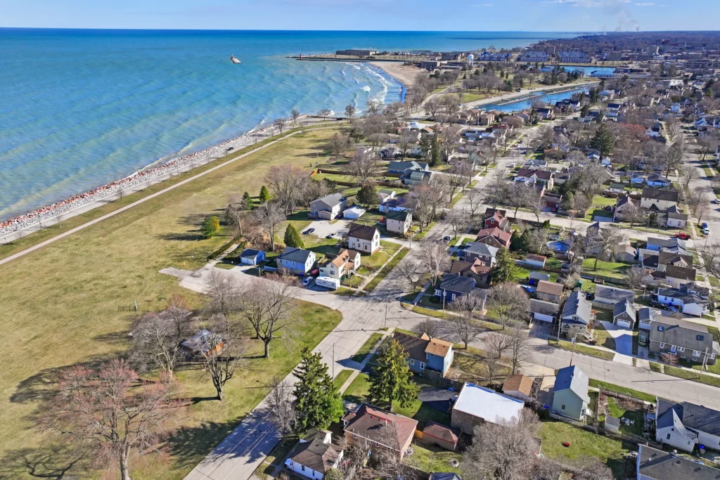 Aerial view of a residential neighborhood bordering a coastline with a long beach and a distant harbor