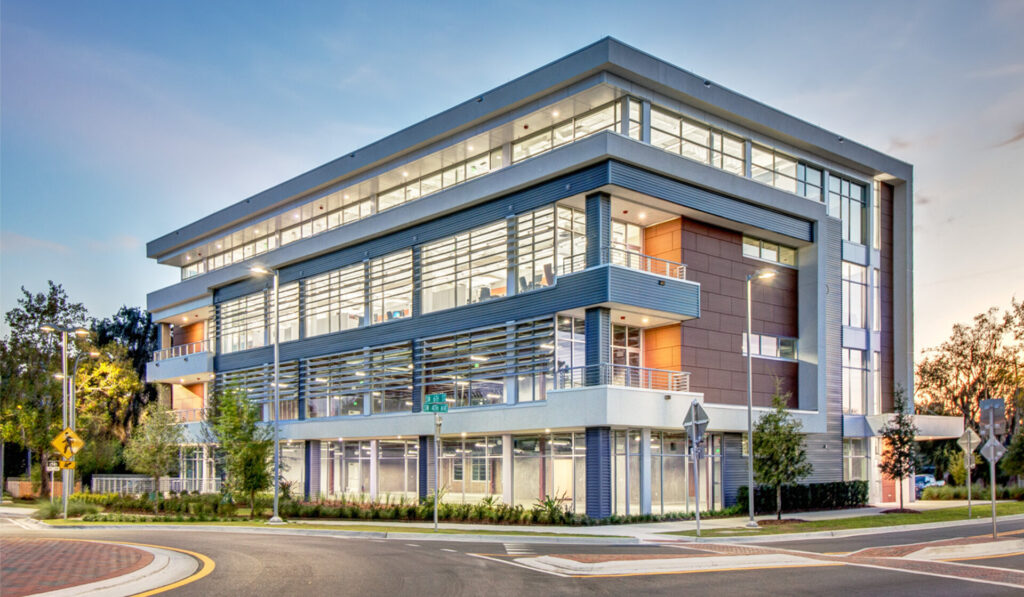Modern four-story office building with glass curtain walls and metal paneling at a street corner intersection