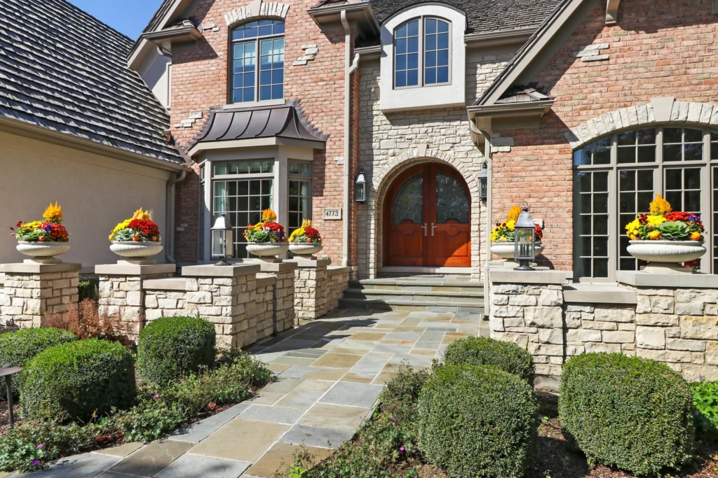 Front entrance of a brick and stone house with a stone walkway and potted flowers