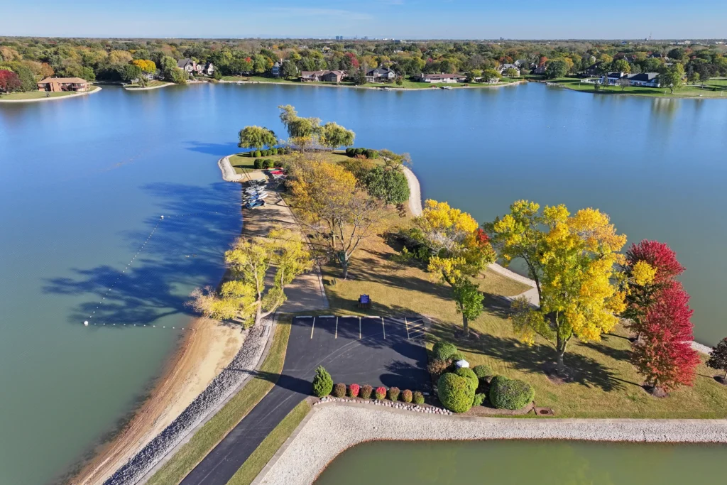 Aerial view of a narrow, tree-lined peninsula extending into a lake, featuring a small parking area and autumn foliage in shades of yellow and red