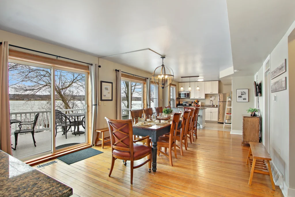Dining area with a wooden table and chairs, hardwood floors, and sliding glass doors opening to a deck overlooking a lake