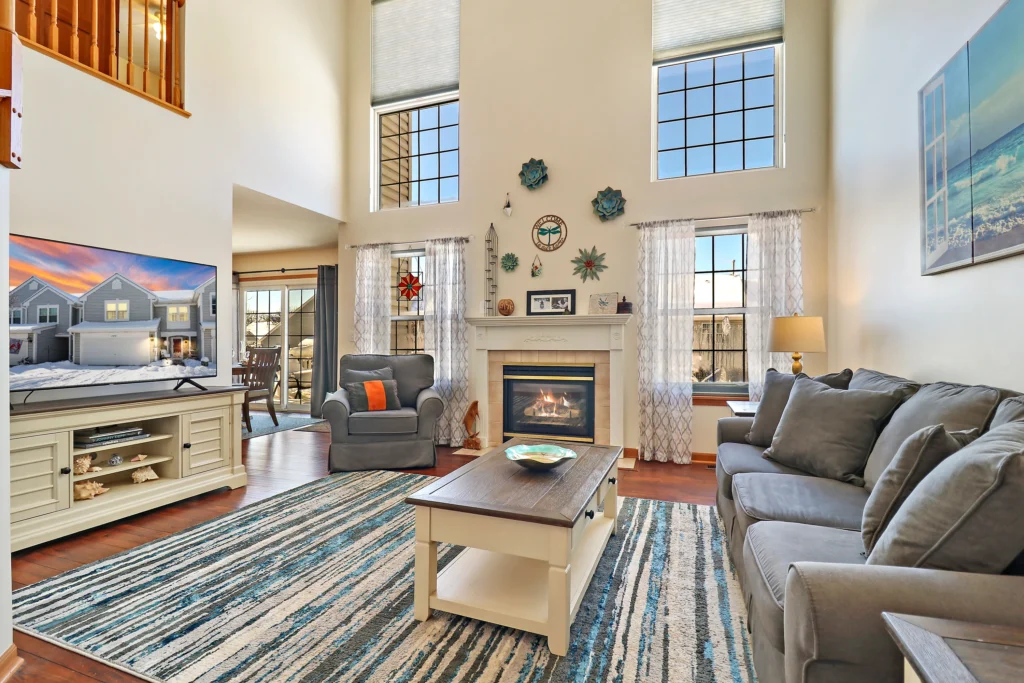 Living room with high ceilings, a fireplace, a large television, and a gray sofa set on a blue and white striped rug