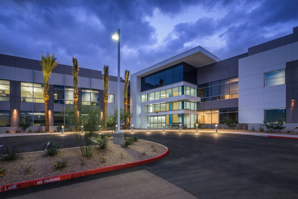 Modern office building exterior at twilight with palm trees and a circular driveway