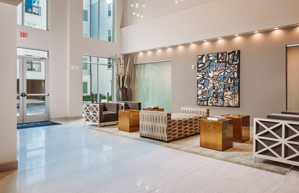 Modern apartment building lobby with high ceilings, large windows, contemporary seating, and abstract wall art